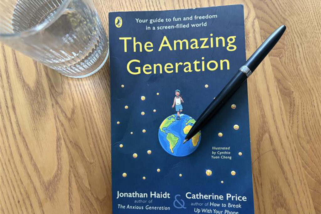 The Amazing Generation book by Jonathan Haidt and Catherine Price - teen phone addiction guide on wooden table with water glass and pen