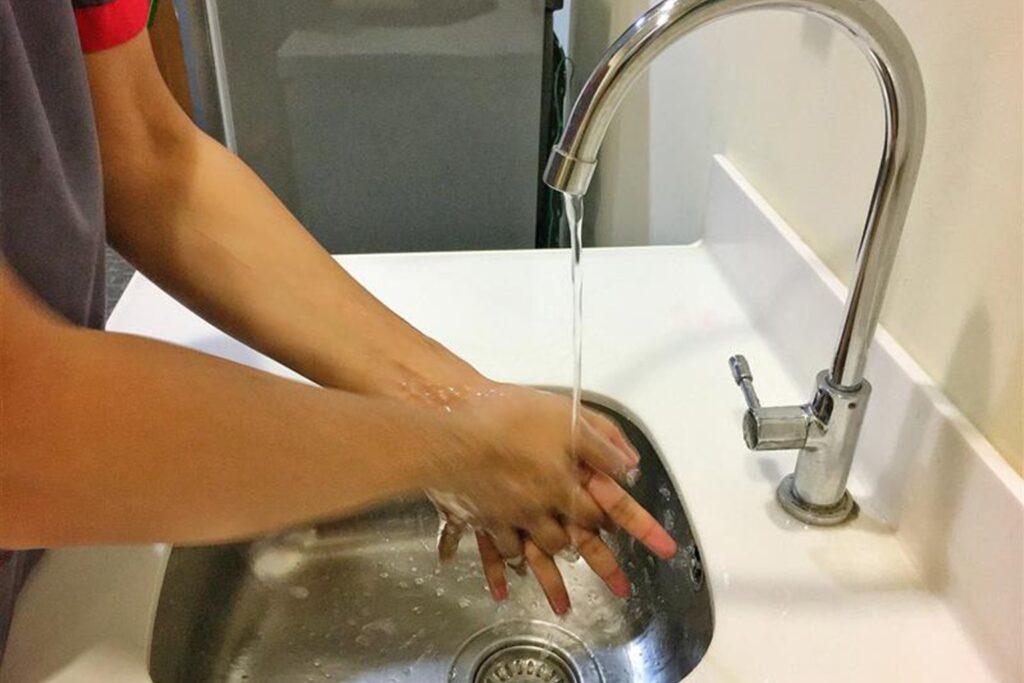 Handwashing under tap water in steel sink — the easiest non-toxic living practice to protect against microbial contamination from everyday cash and thermal receipts