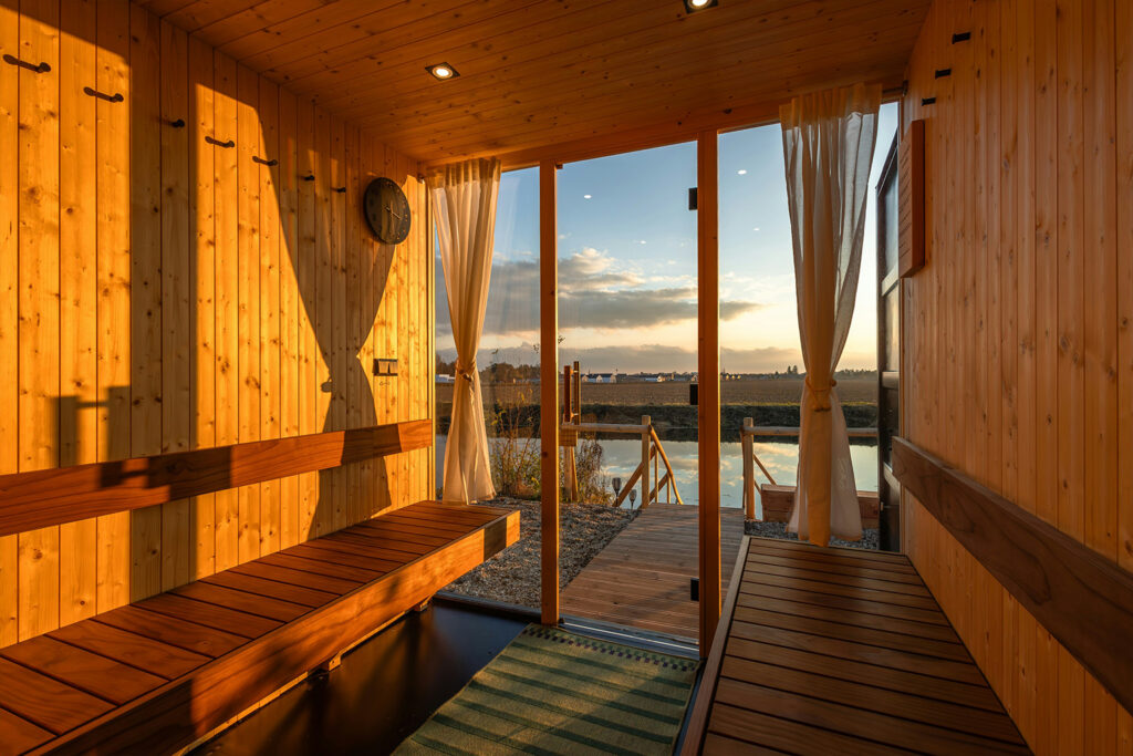 Peaceful traditional Finnish sauna with natural wood benches and sunset view through glass doors - timeless health benefits