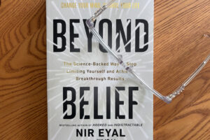 Copy of Beyond Belief by Nir Eyal on a wooden table with reading glasses, representing mindset shifts and behavior change
