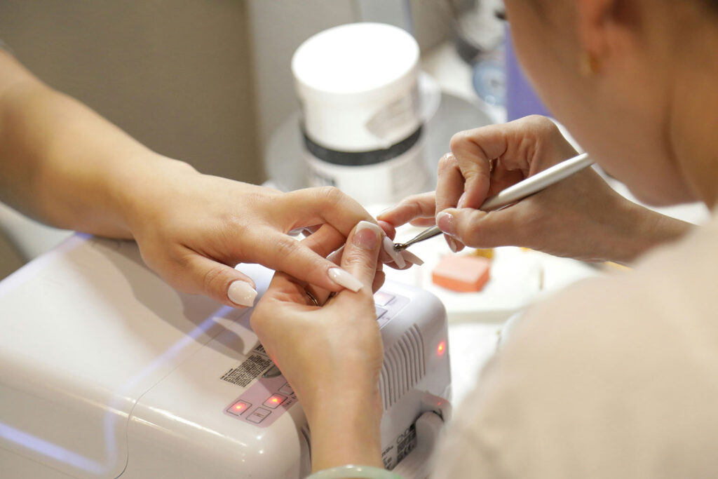 Professional nail technician performing a manicure in a salon without gloves